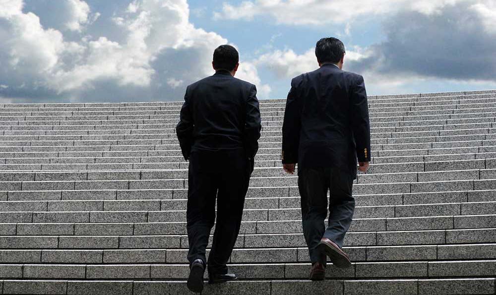 Twee mannen die een trap oplopen met een bewolkte lucht op de achtergrond.